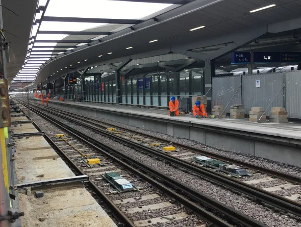 An empty track and people in orange hi-vis jackets at Waterloo East station