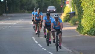 Four men in blue cycling jersey's ride bikes along a road.
