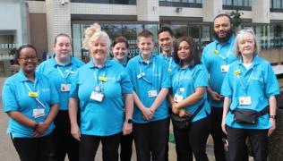 Picture shows the Patient and Staff Enhancers (PASE) team standing outside St Thomas' Hospital. They are wearing blue staff tops and are smiling.