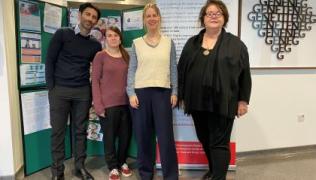 Four members of the research team are standing in front of a display board which has information about research and development at the Trust.