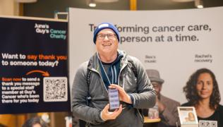 Steve Weiner, smiling, at Guy's Cancer Centre. He is holding a phone which has the distance walked recorded. 