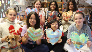 Seven students smiling at the camera holding paper mache hearts