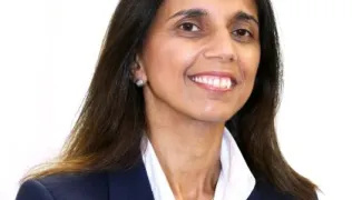 Headshot of Avey, wearing a navy jacket and white shirt. She has long, dark hair and is smiling into the camera.