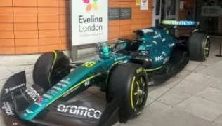 A green Aston Martin Formula One car parked outside of the Evelina London Children's Hospital main entrance