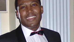 A man wears a black jacket, white shirt and black bow tie