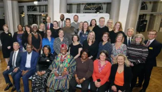A group of approximately 30 people are sitting and standing in a hall