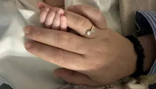 Atlas's finger holding onto Tansy's with a ring on it. 