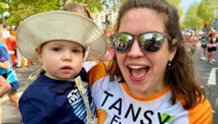 Tansy holding Atlas in her running clothes smiling at the camera after finishing the marathon