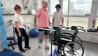 Amputee patient using the bars and supported by two members of staff
