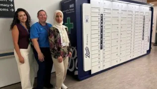 Three pharmacy staff members stand next to the bank of lockers, which have Boots and Guy's and St Thomas' branding on their ends.