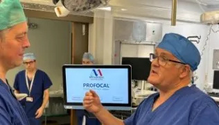 Rick Popert and BBC journalist speaking in front of a ProFocal machine in surgical scrubs.