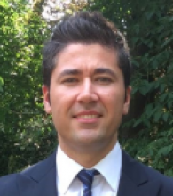 Taner Kasapoglu has short black hair and is wearing a suit