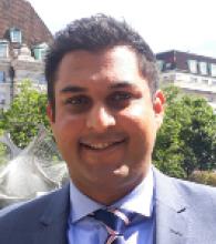 Ash Patel is a man with short black hair and is wearing a suit