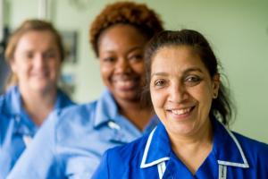 3 female and ethnically diverse nurses wearing blue uniform smile at the camera
