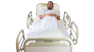 A man wearing a hospital gown lies in a hospital bed