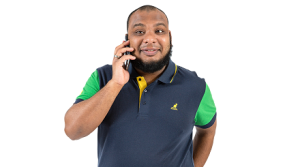 A Black man with a beard dressed in a casual T-shirt holds a mobile to his ear and smiles