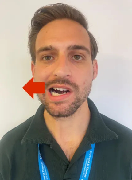 Photo of a man in an upright posture. He has his mouth slightly open and is moving the bottom jaw to the right.