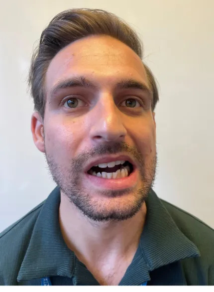 Photo of a man in an upright posture moving his bottom jaw in an anticlockwise direction. This movement replicates a sideways figure of 8 or camel chewing motion.