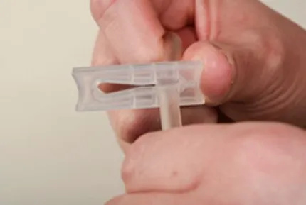 A close-up of hands sliding the plastic clip so the narrow side is clipping the tube closed