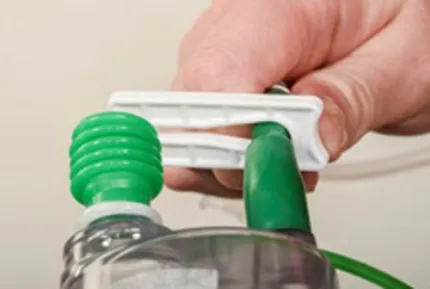 A close-up of a hand sliding the plastic clip at the top of the bottle so the open side is around the tube.