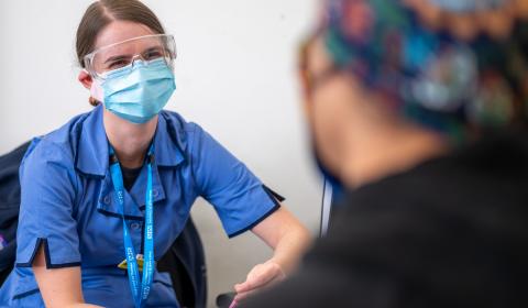 A nurse wearing PPE listening to a patient