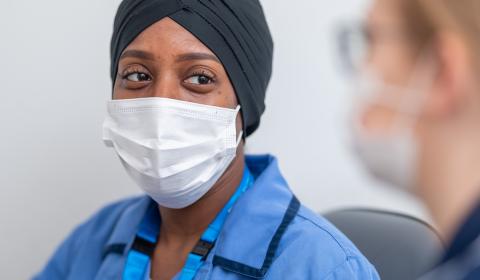 A nurse wearing a face mask talking to a colleague
