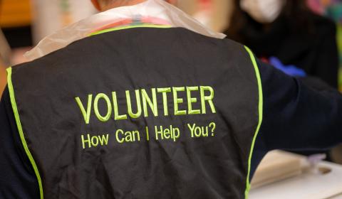 A person wearing a tabard with' volunteer, how can I help you?' on the back
