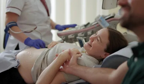 Pregnant person having an ultrasound scan at St Thomas' Hospital, holding her partner's hand and smiling up at the monitor.