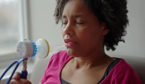 A woman in labour holds a device containing gas and air. Her eyes are closed as she focuses on her breathing.