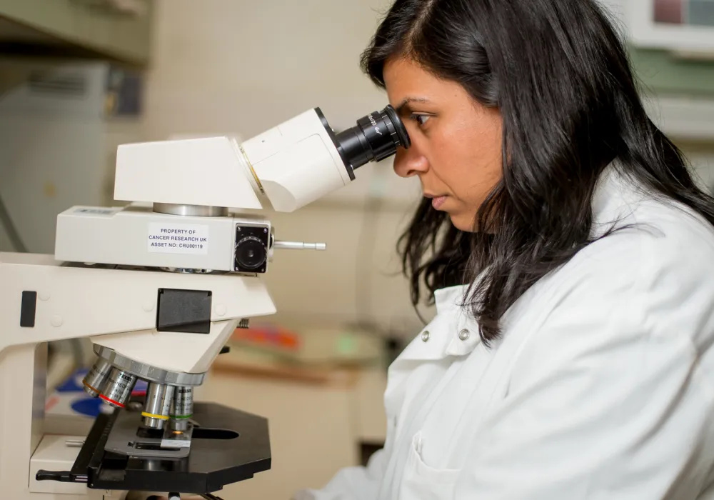 Female Biobank researcher in white lab coat looking into microscope
