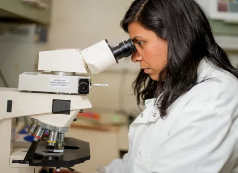 Female Biobank researcher in white lab coat looking into microscope
