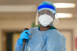 Mary Afriyie, housekeeping assistant, wearing full PPE face shield, mask and apron, with mop
