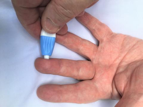 Photo of a hand holding a BD Microtainer lancing device between the thumb and finger, and pressing it against a fingertip