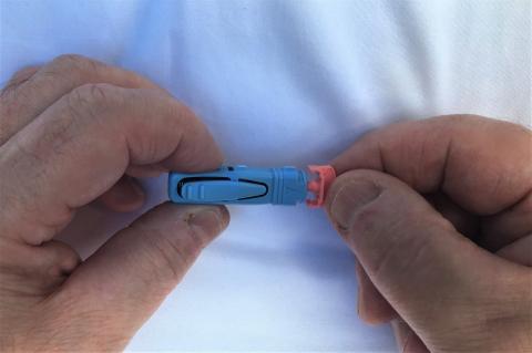 2 hands hold the Unistick 3 lancing device (a blue stick-like tool) from the sides and twist the orange cap