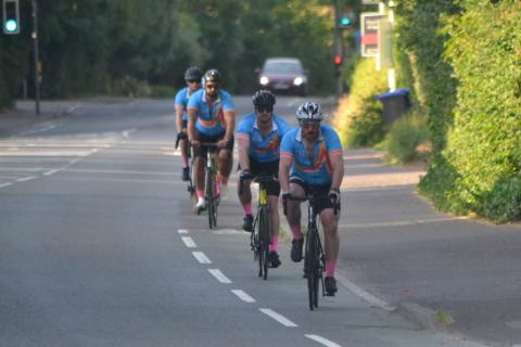 Four men in blue cycling jersey's ride bikes along a road.