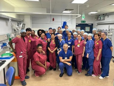 A group photo of the surgical and theatre teams who did the Aquablation HIT list. They are standing or crouching in a clinical area at Guy's Hospital, wearing blue or maroon scrubs .