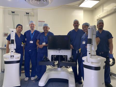 Members of the surgical team stand next to the Versius robotic system