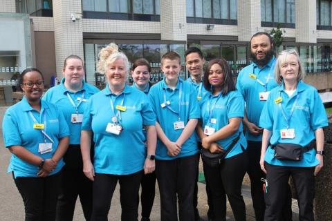 Picture shows the Patient and Staff Enhancers (PASE) team standing outside St Thomas' Hospital. They are wearing blue staff tops and are smiling.