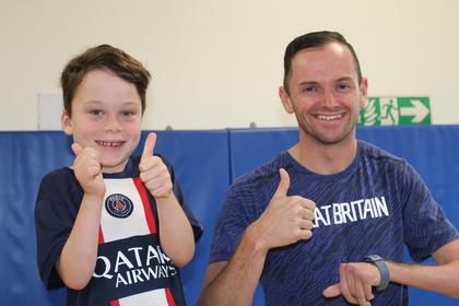A child and a man smiling at the camera, with their thumbs up 