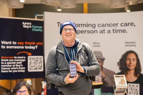 Steve Weiner, smiling, at Guy's Cancer Centre. He is holding a phone which has the distance walked recorded. Photo credit: Simon Roberts. 