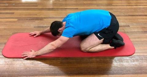Person easing bottom to rest on feet. Arms straight in front and head down.