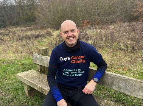 Gary Richardson is sat on a bench, smiling. He is wearing a Guy's Cancer Charity t-shirt. 