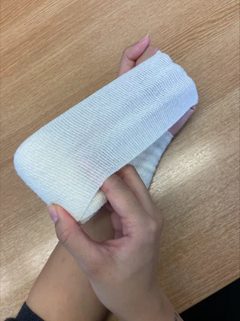 Photo of someone's hands and left forearm. A white bandage has been wrapped around their left wrist. The right hand is holding the roll of bandage, which stretches above the person's left fingers and down their forearm.