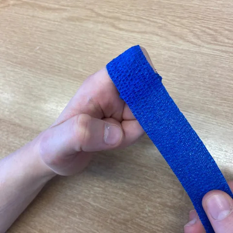 Photo of a long, thin dark blue bandage. One end is wrapped around a bent left index finger and the right hand holds the other end.