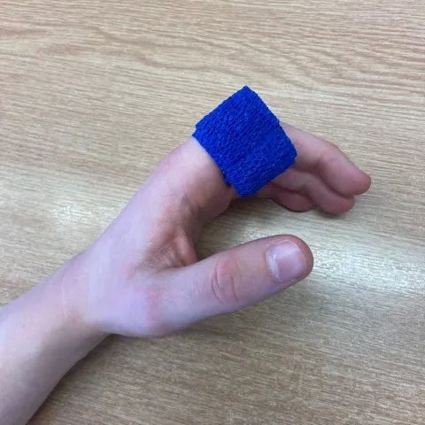 Photo of a dark blue bandage wrapped several times around the index finger of someone's hand.