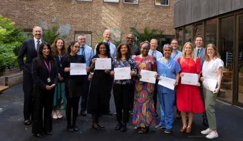 Group of staff posing together in a courtyard with members of staff at the front holding certificates
