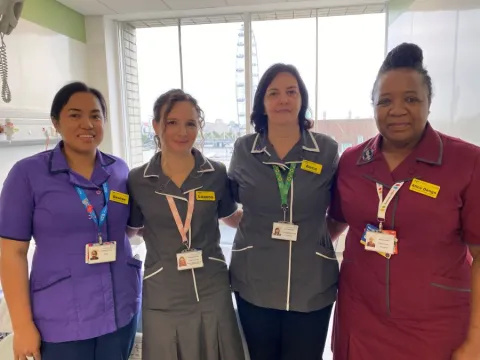 Four nurses stand shoulder to shoulder in a hospital room