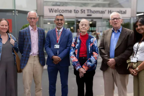 Six individuals standing outside the main entrance of St Thomas' Hospital. They are smiling at the camera.
