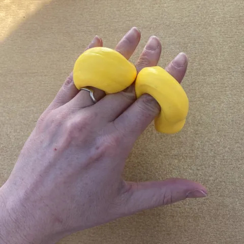Photo of someone's hand with a yellow rope of putty wound between their fingers. They are squeezing their fingers together, whilst keeping the fingers straight.