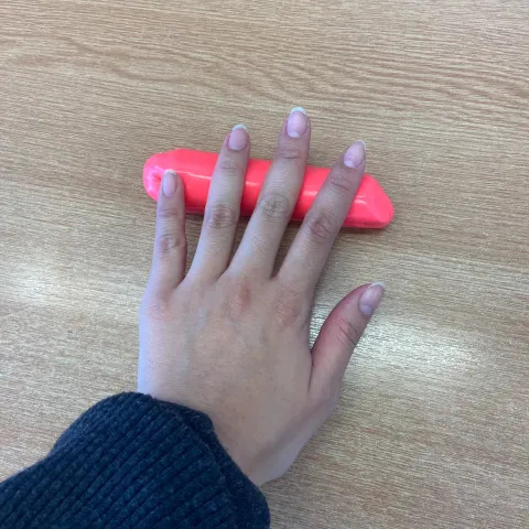 Photo of someone's outstretched hand with some red putty that they are rolling into a long cylinder shape beneath their fingertips.
